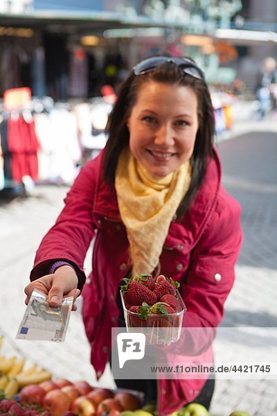 Junge Frau Zahlung für Korb mit Erdbeeren