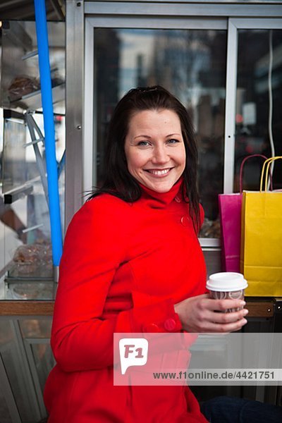 Portrait of junge Frau hält Takeaway Kaffee  mit Einkaufstüten im Hintergrund