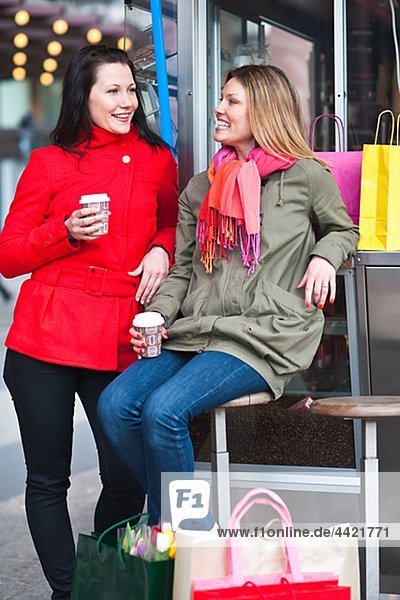 Pair of young women taking break from shopping  drinking takeaway coffee