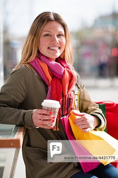 Portrait of young woman with coffee cup and shopping bag