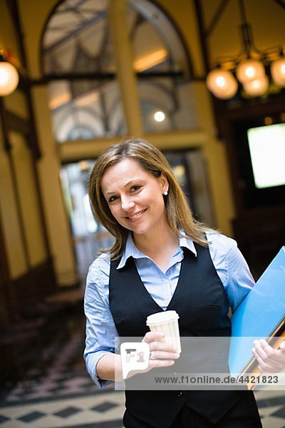 Portrait of mid-adult businesswoman holding file and takaway coffee
