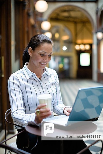 Reife geschäftsfrau arbeiten auf Laptop  halten Kaffee zum Mitnehmen