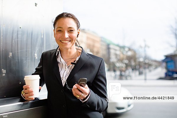 Porträt von fröhlich geschäftsfrau mit Takeaway Kaffee in einer Hand und Handy in einem anderen