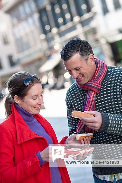 Mid adult couple eating sausages on street