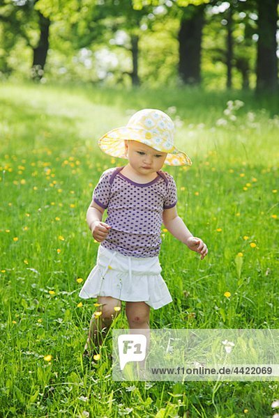 Girl wearing sun hat walking through meadow