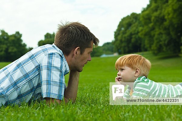 Father and son lying on lawn in park