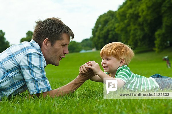Vater und Sohn liegend auf Rasen im Park und spielen