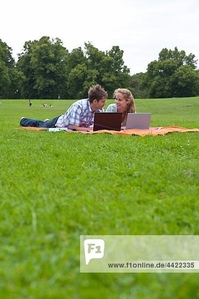 Mitte adult Paar auf Rasen im Park liegen und mit laptops