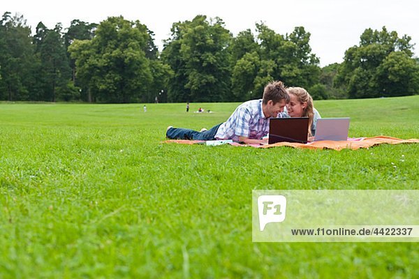 Mid adult couple lying on blanket in park with laptops