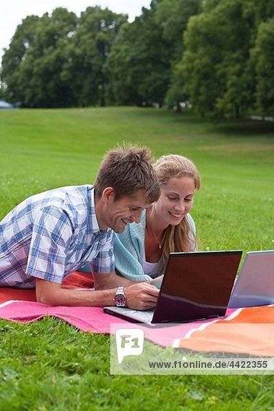 Mid adult couple lying on blanket with laptops
