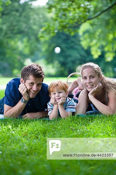 Eltern mit Sohn im Park liegen und Blick in die Kamera