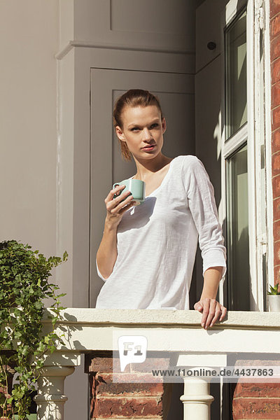Young woman holding cup at window