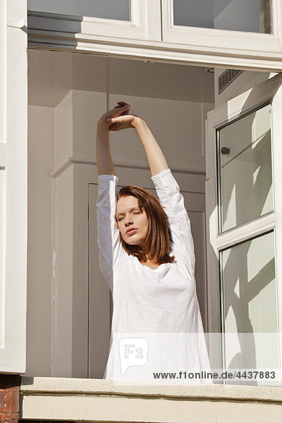 Young woman stretching at window