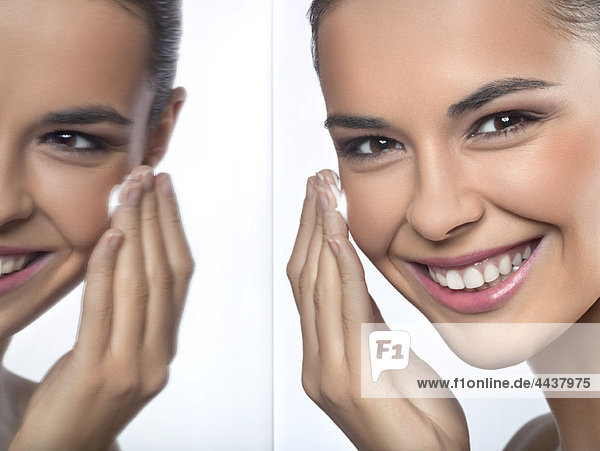 Young woman applying moisturizer and her reflection in mirror