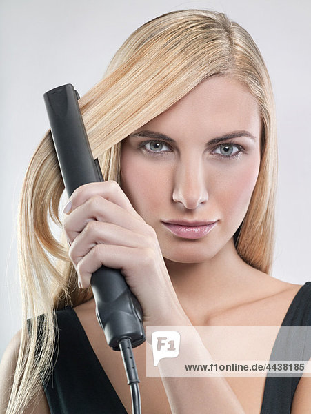 Young woman using hair straighteners