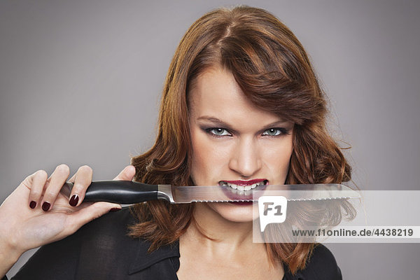 Junge Frau mit Messer zwischen den Zähnen