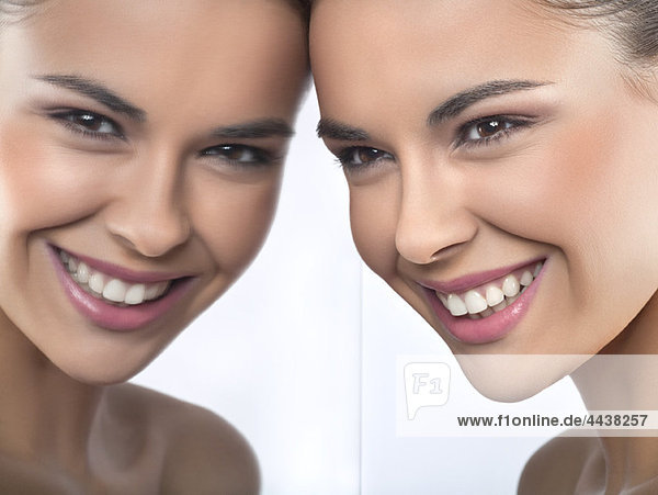 Junge Frau lächelt und spiegelt sich im Spiegel.