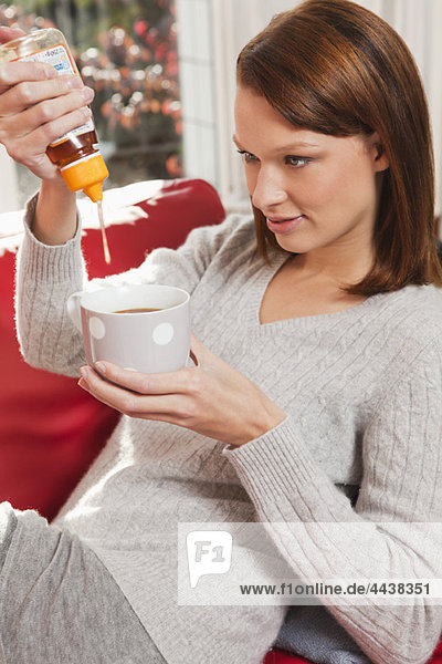 Young woman pouring honey into her tea cup