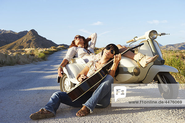 Women resting by road with motorbike