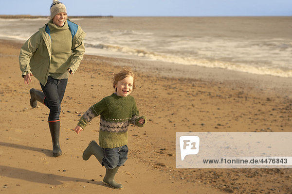 Frau  kleiner Junge  der am Strand rennt. Herbst