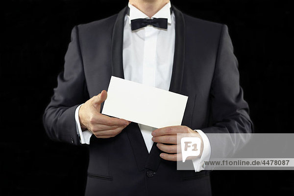 Mittelteil eines Mannes  der einen Smoking trägt und einen Umschlag hält.
