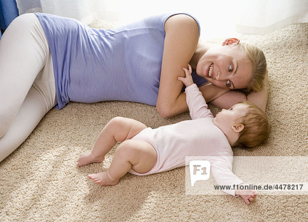Eine Mutter und ihr Baby liegen auf einem Teppichboden.