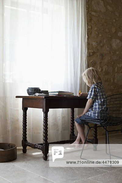 Ein Junge  der an einem Schreibtisch sitzt.