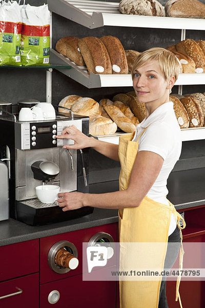 Eine Verkäuferin  die eine Espressomaschine in einem Bäckerei-Café benutzt.