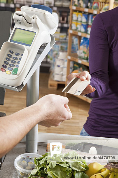Ein Kunde  der einer Kassiererin eine Kreditkarte im Supermarkt übergibt.