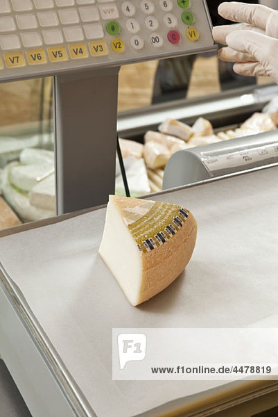A wedge of cheese being weighed on a delicatessen scale