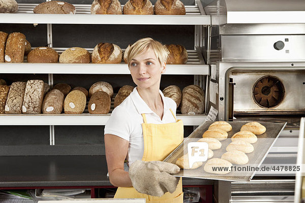 A woman pulling a tray of freshly baked rolls in a bakery