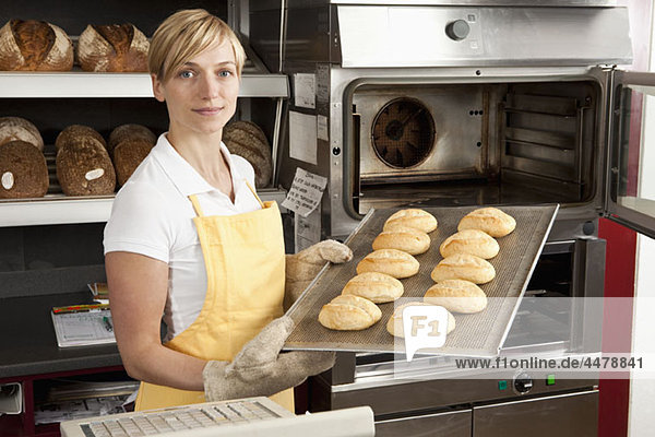 A woman pulling a tray of freshly baked rolls in a bakery