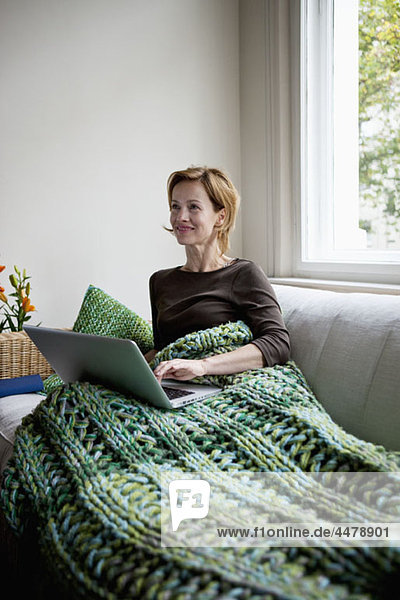 Eine Frau  die auf einer Couch liegt und einen Laptop benutzt.