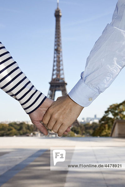 A man and woman holding hands in front of the Eiffel Tower  focus on hands