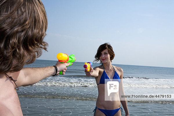 Ein junges Paar spielt am Strand mit Spritzpistolen.