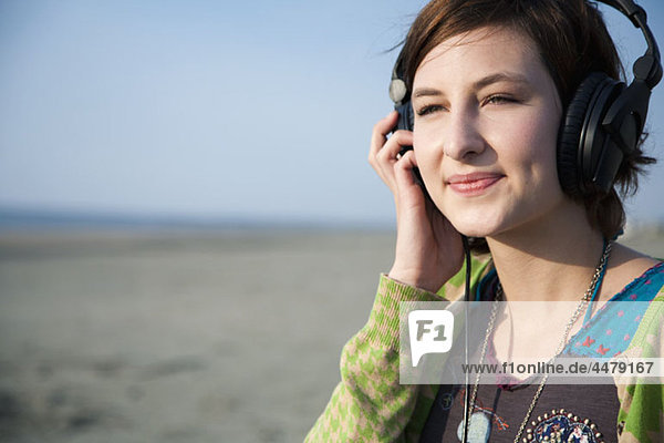 Eine Frau  die am Strand Kopfhörer hört.