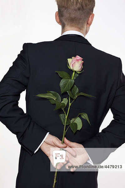 Ein Mann hält eine Rose hinter seinem Rücken  Rückansicht  Taille hoch.