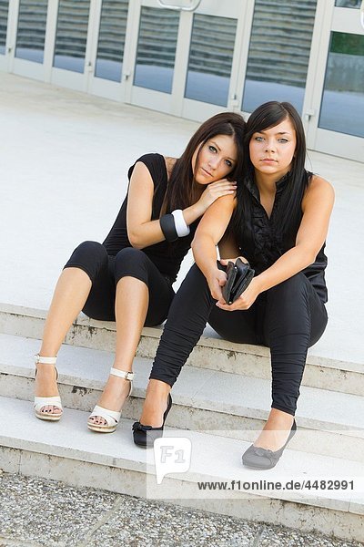 Two young women are sitting on the street