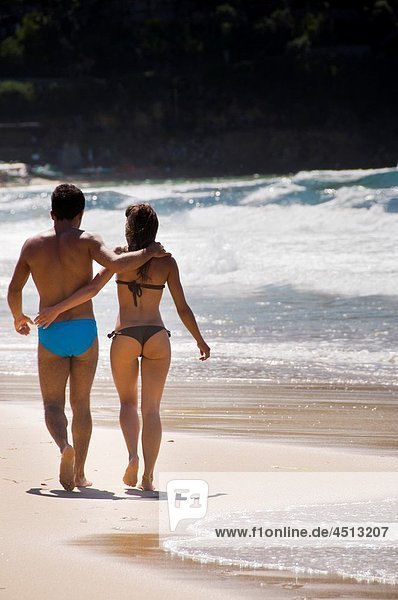 A couple in bathing suits walking together on the beach  rear view