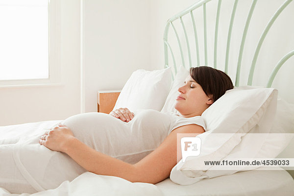 Eine schwangere Frau schläft im Bett.