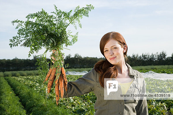 Young woman holding bunch of carrots in field