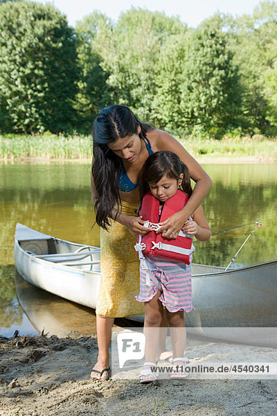 Mother putting lifejacket on daughter