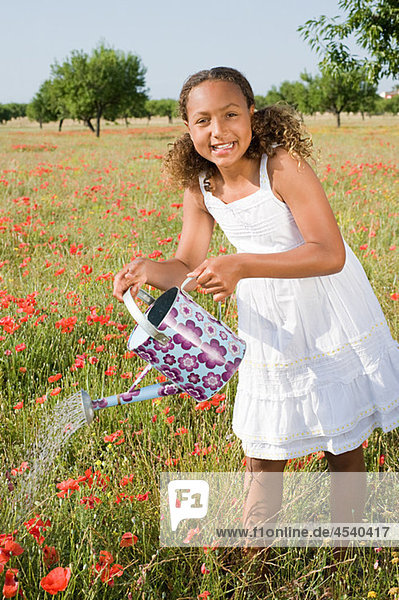 Young girl watering poppy field with watering can