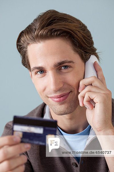 Junger Mann am Telefon mit Kreditkarte