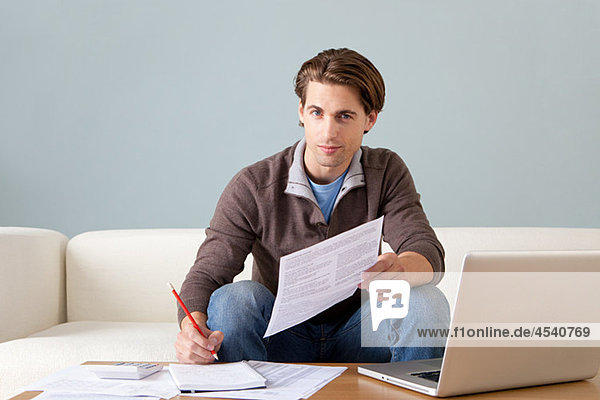 Young man with paperwork using laptop