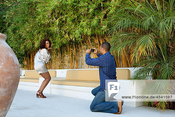 Man taking a picture of girlfriend as she blows a kiss to camera