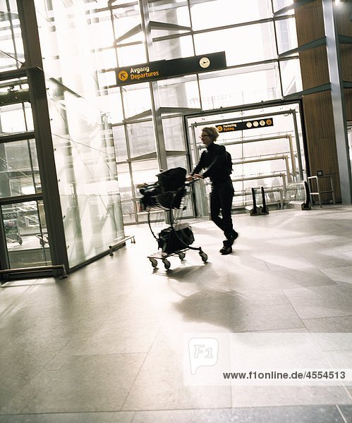Frau drängen Gepäckwagen am Flughafen