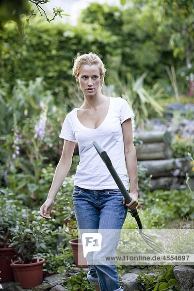 Young woman carrying pitchfork in garden