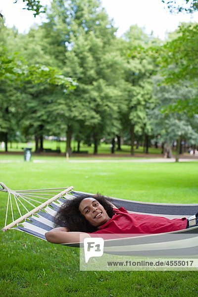 Young man with afro hair lying in hammock in park