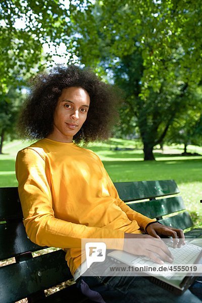 Junger Mann mit Afro Haar auf Bank mit Laptop sitzen